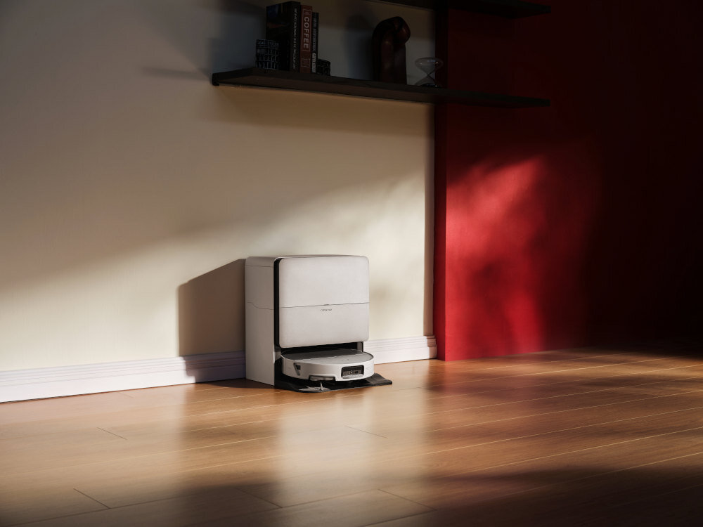 Na drewnianej podłodze stoi biały robot sprzątający z napisem \'ROBOROCK\'. W tle widać jasną ścianę z półką, na której znajdują się książki i dekoracje.