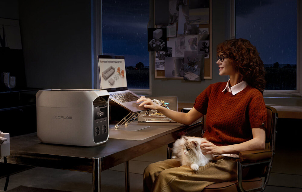 Na biurku znajduje się stacja zasilania z widocznym logo \'ECOFLOW\'. Obok siedzi osoba z laptopem, na którym widoczny jest tekst \'Future Engineering Diagram\'.