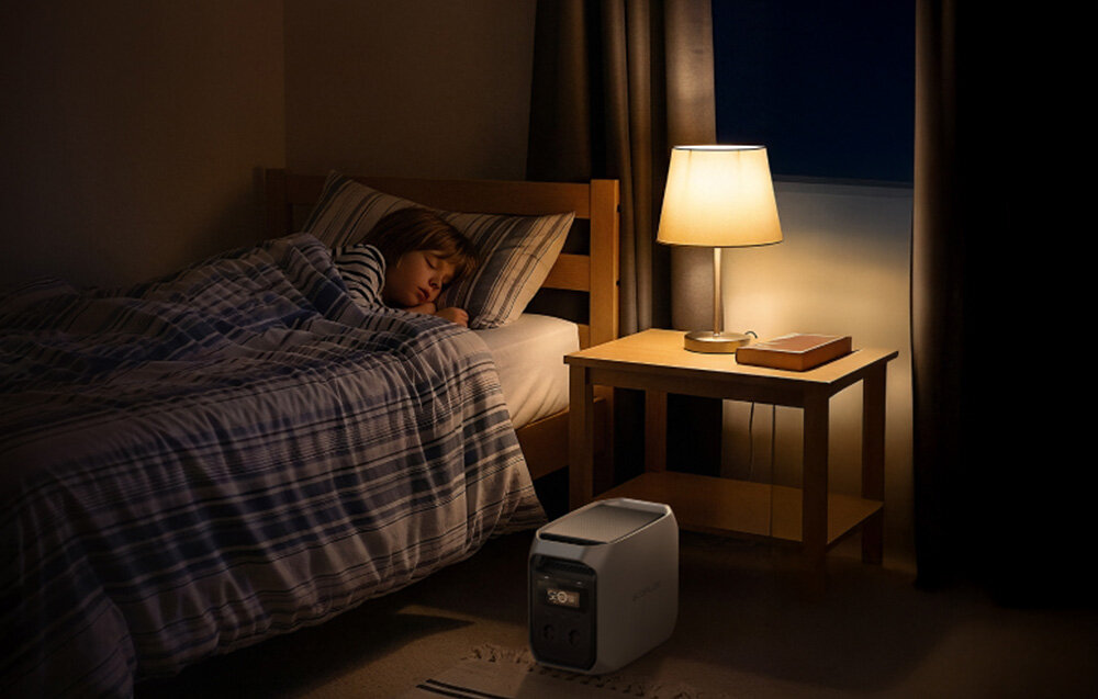 Osoba śpiąca w łóżku obok stolika nocnego z lampką i książką. Na podłodze stoi stacja zasilania ECOFLOW.