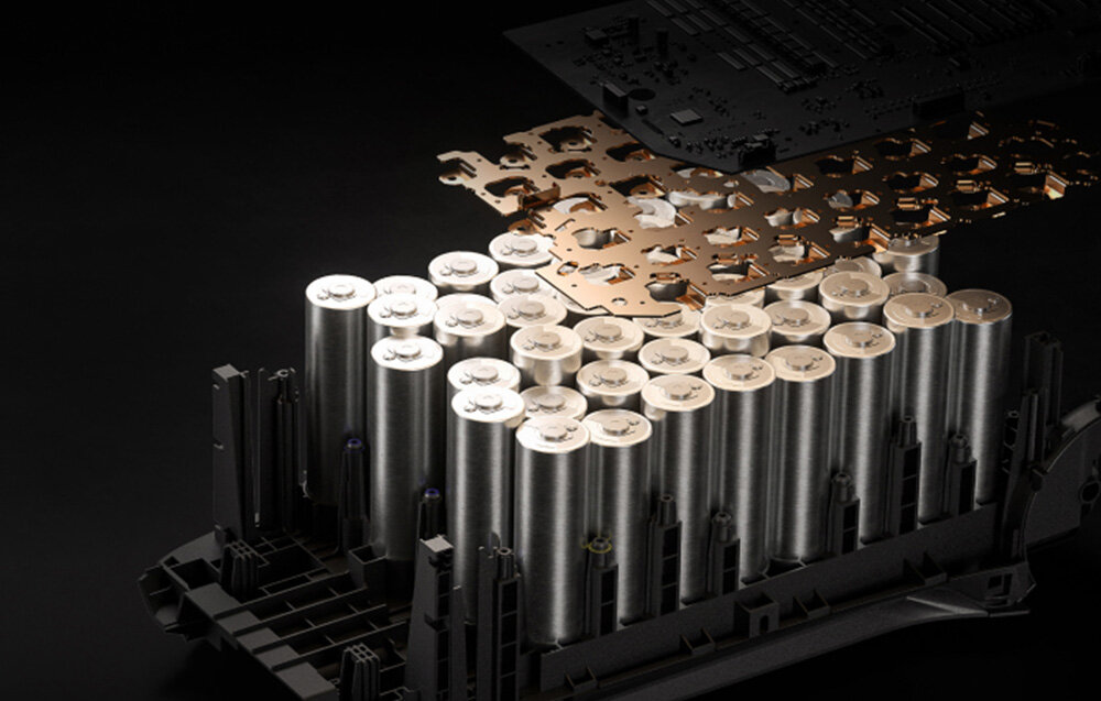 Obraz przedstawia wnętrze urządzenia z widocznymi cylindrycznymi ogniwami baterii ułożonymi w rzędach. Nad nimi znajduje się metalowa płytka z wycięciami, a w tle widoczna jest płytka drukowana.