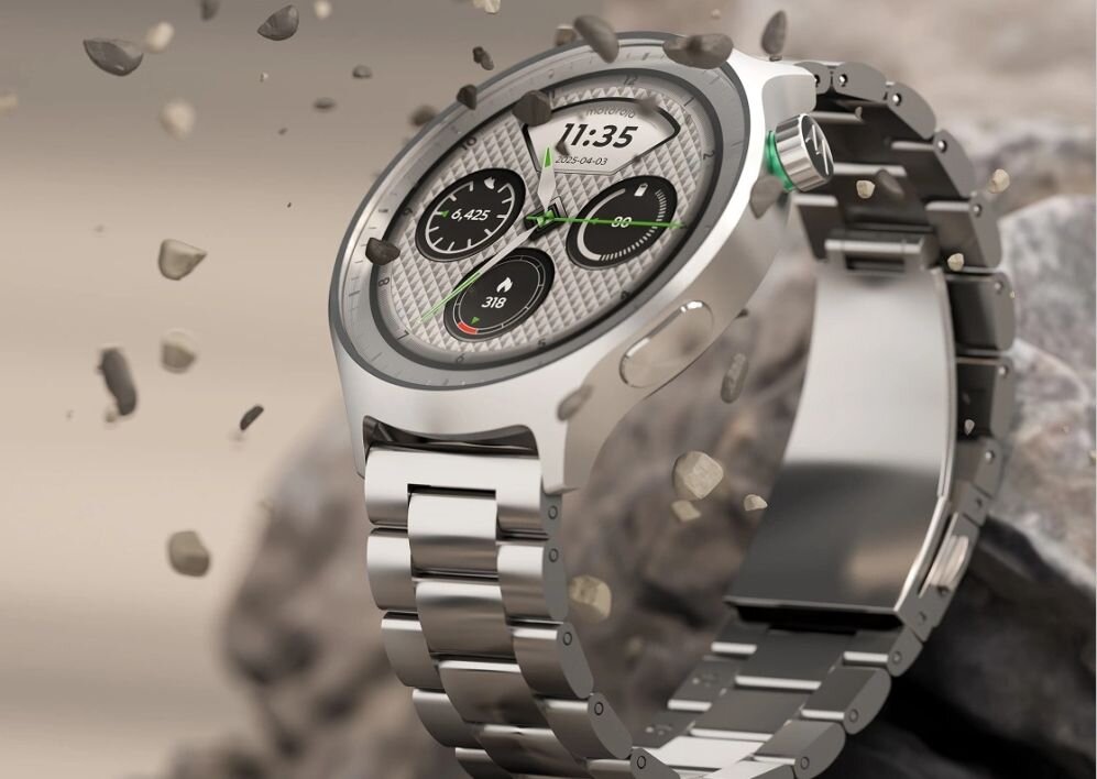 Smartwatch z metalową bransoletą i okrągłym wyświetlaczem, na którym widoczne są trzy małe tarcze oraz godzina 11:35. W tle unoszą się drobne kamienie.
