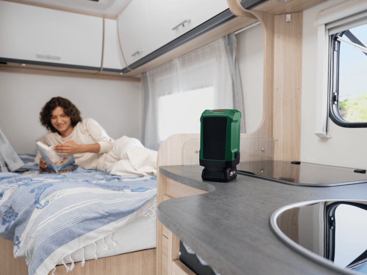Głośnik mobilny BOSCH UniversalSpeaker 18V-1 06039G5000 Zielono-czarny, multi-speaker, bluetooth, parowanie, system, Głośnik w kamperze obok kobiety czytającej książkę.