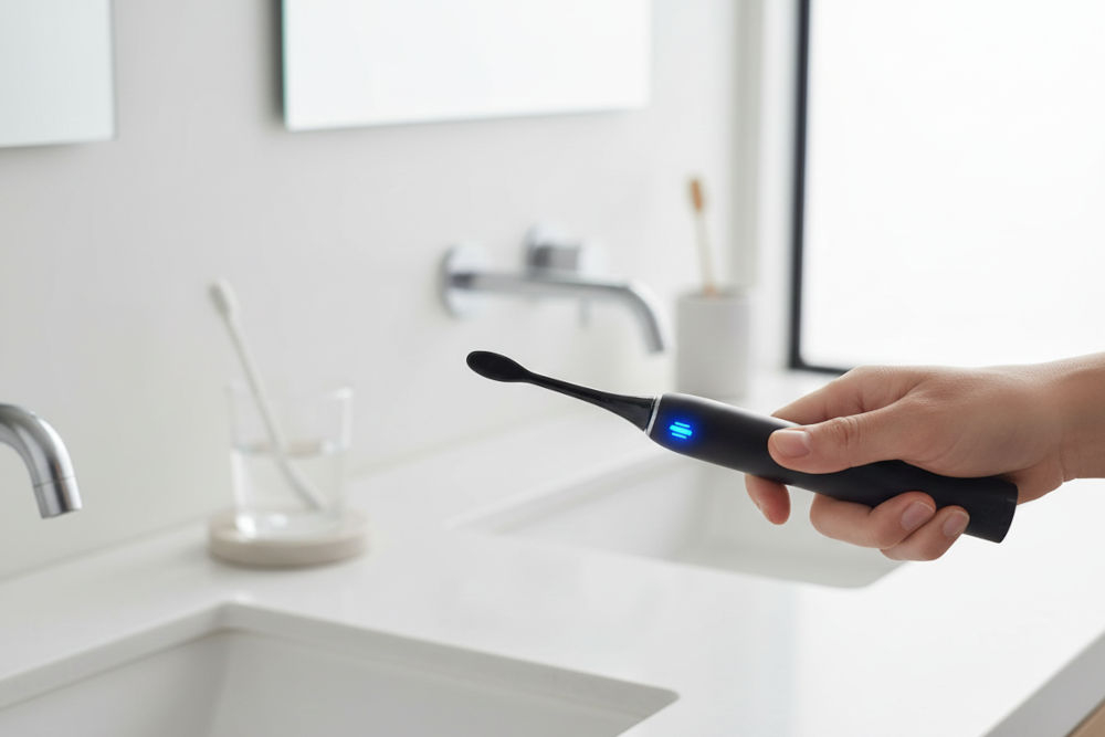 Szczoteczka soniczna GÖTZE & JENSEN ST955 czujnik nacisku sygnalizacja LED trzy poziomy naładowania kontrola mocy tryby pracy Dłoń trzymająca czarną szczoteczkę soniczną Götze & Jensen z aktywnym, niebieskim podświetleniem wskaźnika.