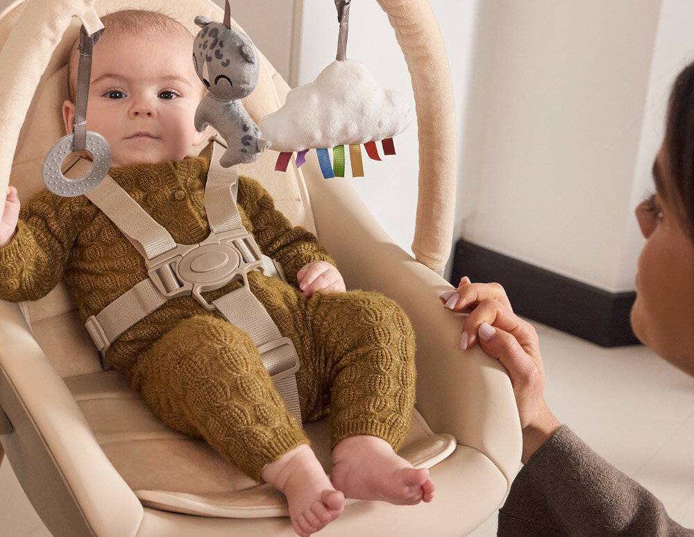 Krzesełko do karmienia KINDERKRAFT Fini Up 2w1 Beżowy Trzy tryby użytkowania 3w1 leżaczek dla noworodka krzesełko do karmienia miejsce dla starszego dziecka dziecko patrzy w obiektyw osoba patrzy na dziecko i trzyma rękę na krzesełku