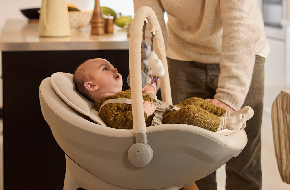 Krzesełko do karmienia KINDERKRAFT Fini Up 2w1 Beżowy Bezpieczeństwo i stabilność Pięciopunktowe pasy Antypoślizgowe stopki dziecko patrzy na zabawki osoba opiera się o krzesełko