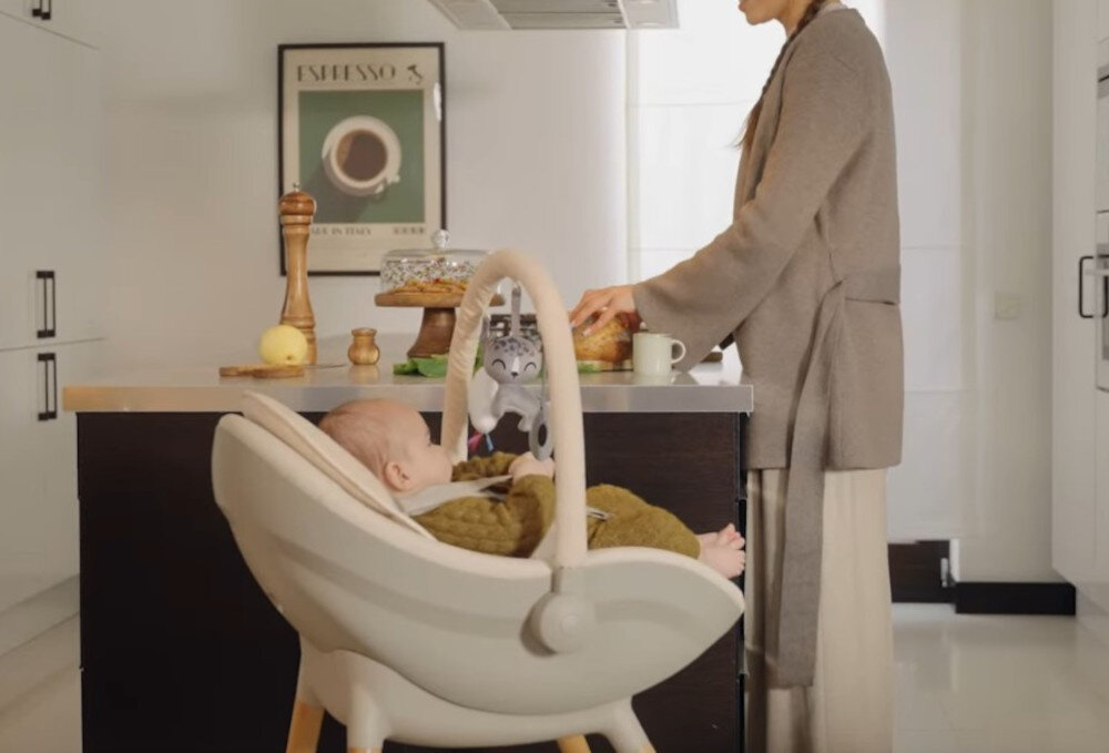 Krzesełko do karmienia KINDERKRAFT Fini Up 2w1 Beżowy Komfort dla najmłodszych  dziecko siedzi ukosem w foteliku osoba krząta się po kuchni Miękka wkładka od pierwszych miesięcy życia