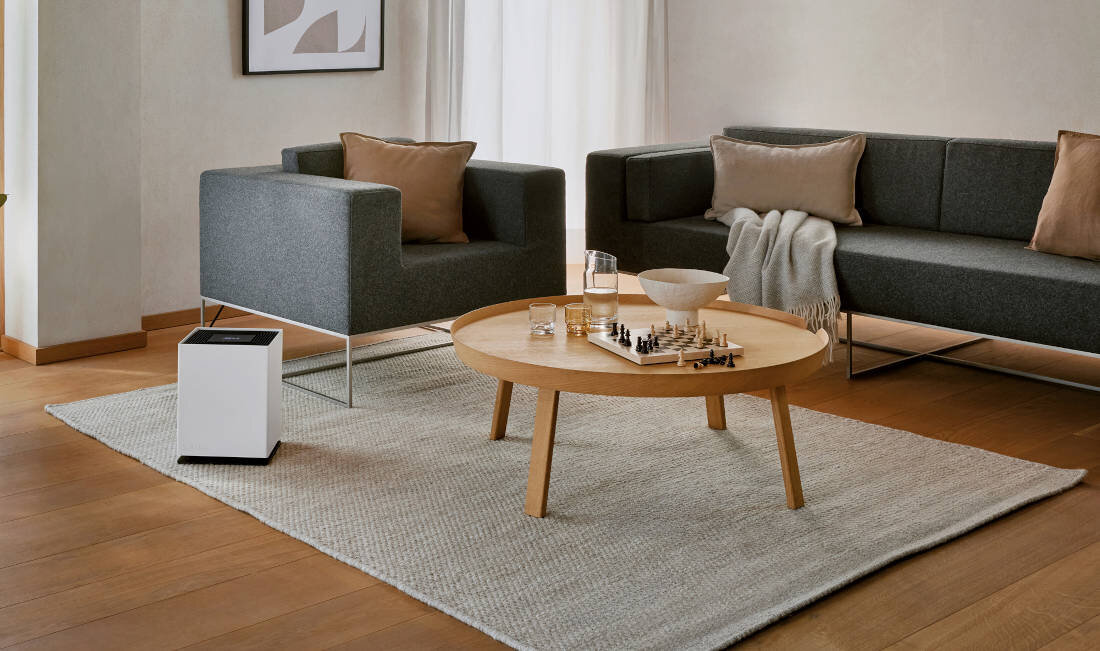 W salonie znajduje się biały nawilżacz ewaporacyjny obok szarego fotela. Na drewnianym stoliku leży szachownica i kilka szklanek.