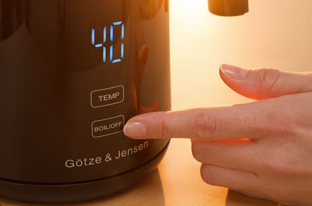 Czajnik GÖTZE & JENSEN KT730K z wyświetlaczem temperatury regulacja 40-100°C do herbaty kawy Zbliżenie na podstawę czarnego czajnika Goetze & Jensen. Wyświetlacz pokazuje 40 stopni. Widoczne są przyciski TEMP i BOIL/OFF. Palec naciska przycisk BOIL/OFF.