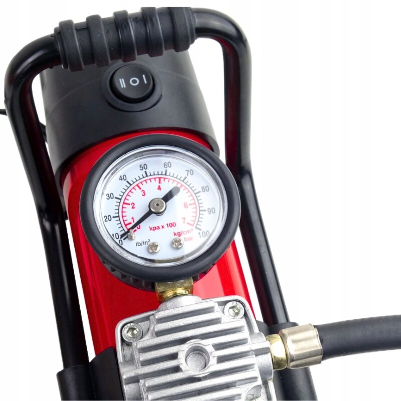 Na obrazie widoczny jest manometr z podziałką do 100 psi, zamontowany na czerwonym kompresorze samochodowym. Obok znajduje się włącznik z oznaczeniem \'I\' i \'O\'.