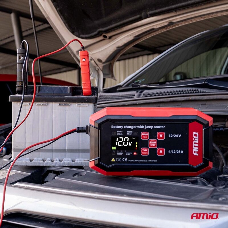 Na obrazie widoczna jest ładowarka do akumulatora z wyświetlaczem pokazującym \'12.0V\', podłączona do akumulatora samochodowego. Na urządzeniu znajduje się logo \'AMiO\'.