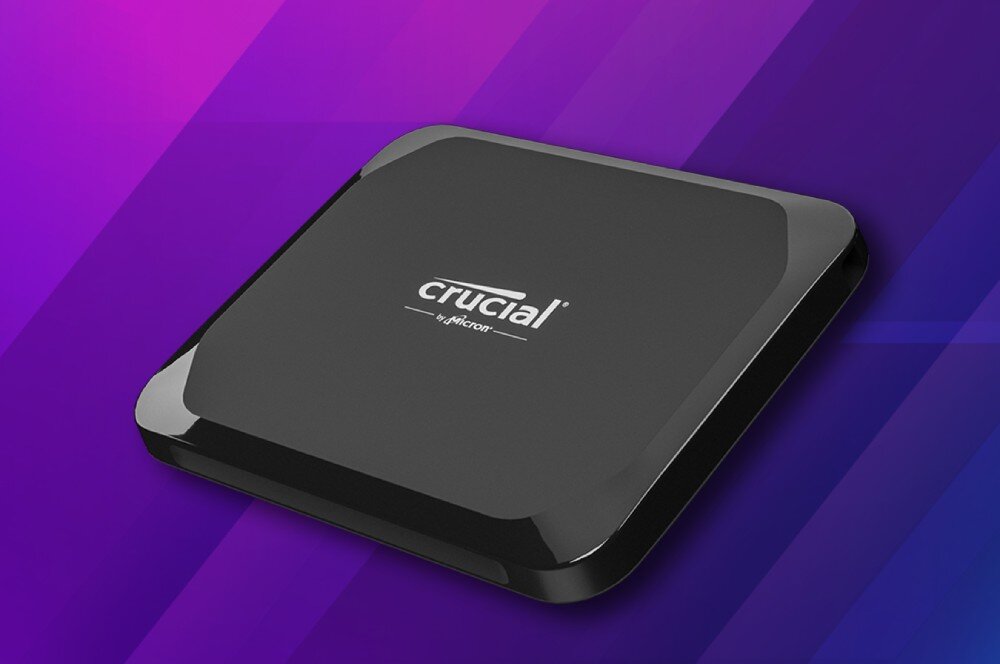 Dysk CRUCIAL X9 Zbliżenie na czarny dysk przenośny z widocznym białym logo producenta na cieniowanym fioletowym tle z geometrycznymi wzorami, wielkość, otwór na smycz, wygląd