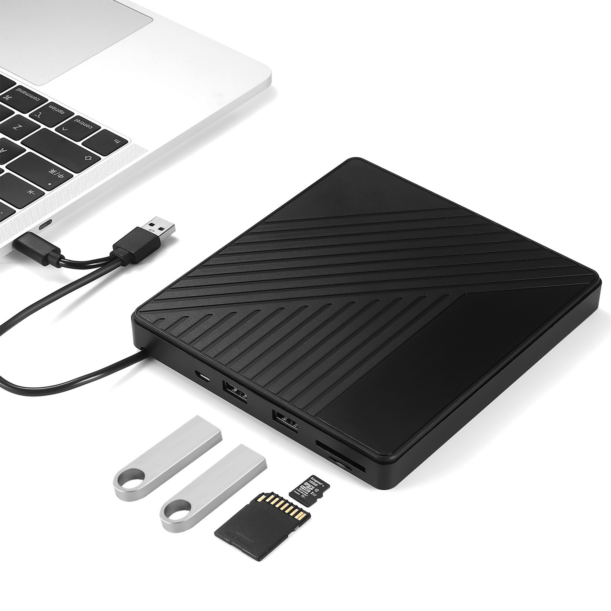 Na obrazie widoczny jest czarny zewnętrzny napęd optyczny z podłączonym kablem USB do laptopa. Obok znajdują się dwa pendrive\'y oraz karta SD i microSD.