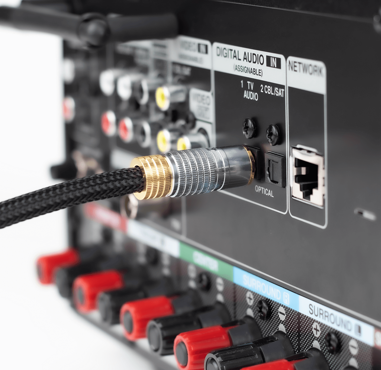 Zdjęcie przedstawia tylny panel urządzenia audio z podłączonym kablem optycznym do portu oznaczonego jako \'OPTICAL\'. Widoczne są również inne złącza audio i sieciowe oraz kolorowe gniazda głośnikowe.