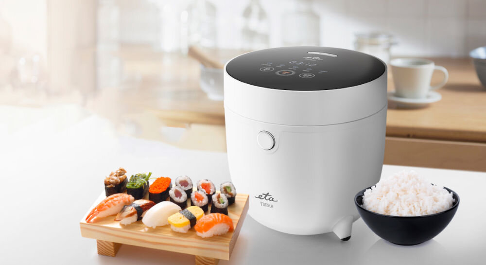 Ryżowar ETA FitRice ETA413990000 Do dań z ryżem ryżowar biała obudowa czarny panel przyciski wyświetlacz jasne tło obok stoi miska z ryżem 