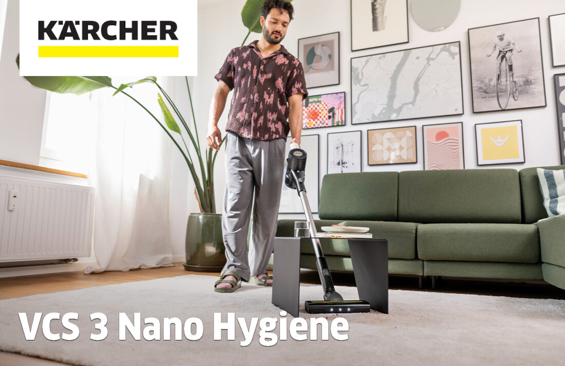 Osoba używa odkurzacza w salonie z zieloną sofą i ścianą ozdobioną obrazami. Widoczne jest logo \'KÄRCHER\' oraz napis \'VCS 3 Nano Hygiene\'.