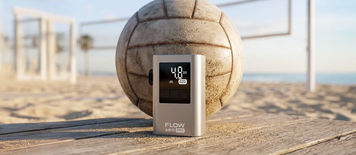 Na drewnianej powierzchni na plaży stoi urządzenie z wyświetlaczem pokazującym \'40 psi\', obok piłki do siatkówki. Na urządzeniu widoczny jest napis \'FLOW AIR12 PRO\'.