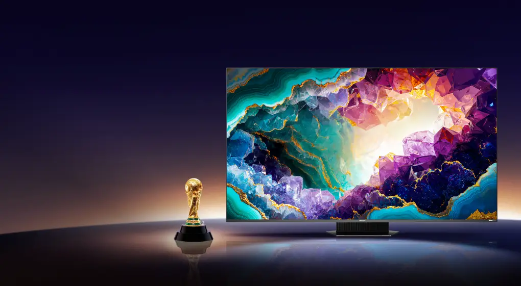 Telewizor z wyświetlaczem pokazującym kolorową grafikę z motywem kryształów. Obok znajduje się złoty puchar na ciemnym tle.