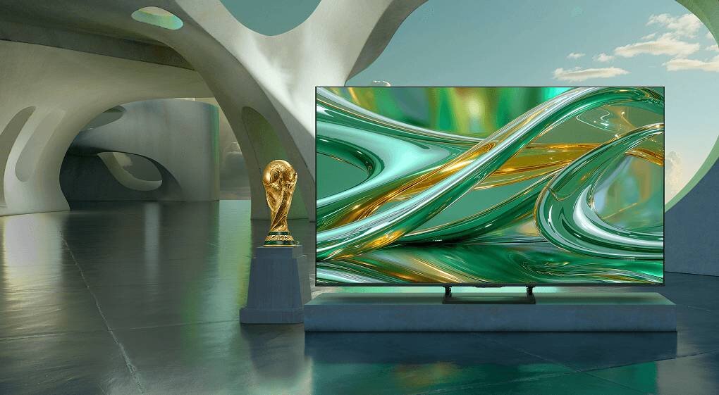 Telewizor z wyświetlaczem prezentującym abstrakcyjne, zielono-złote wzory stoi w nowoczesnym wnętrzu z łukowatymi strukturami. Obok telewizora znajduje się złoty puchar na postumencie.