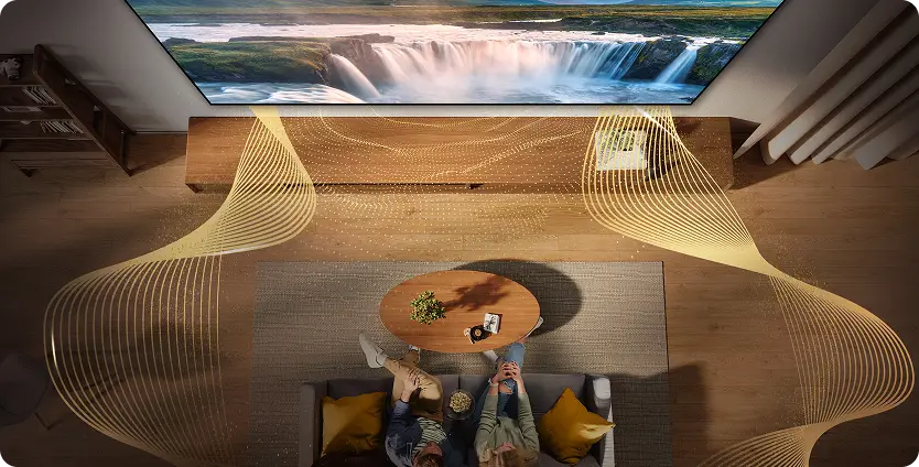 Widok z góry na parę na kanapie; ilustracja złotych fal wokół telewizora symbolizuje dźwięk przestrzenny Dolby Atmos
