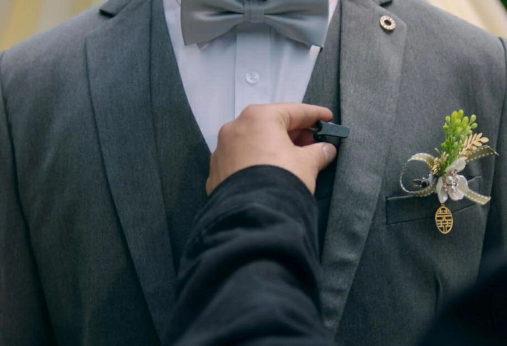 System bezprzewodowy HOLLYLAND Lark Max 2 Ultimate Combo Mężczyzna w garniturze na weselu, któremu ktoś pomaga założyć mikrofon MAX 2 niemal niewidoczny pełen szczegółów dźwięk nagrywanie audio bez kompromisów