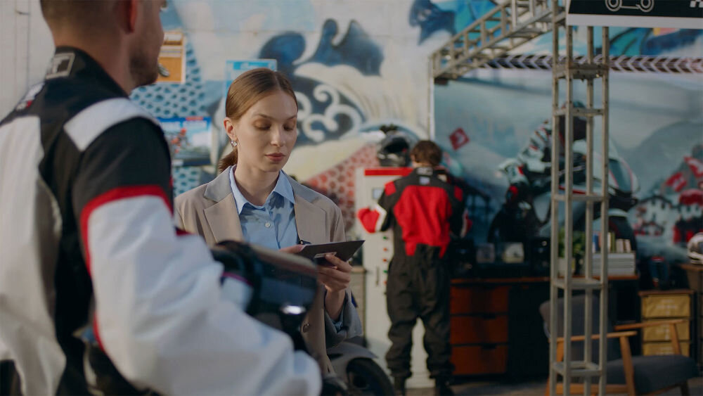 System bezprzewodowy HOLLYLAND Lark Max 2 Ultimate Combo kobieta przeprowadzająca wywiad z motocyklistą w tle warsztat zakres temperatur przystosowany do pracy w plenerze odporność trwałość