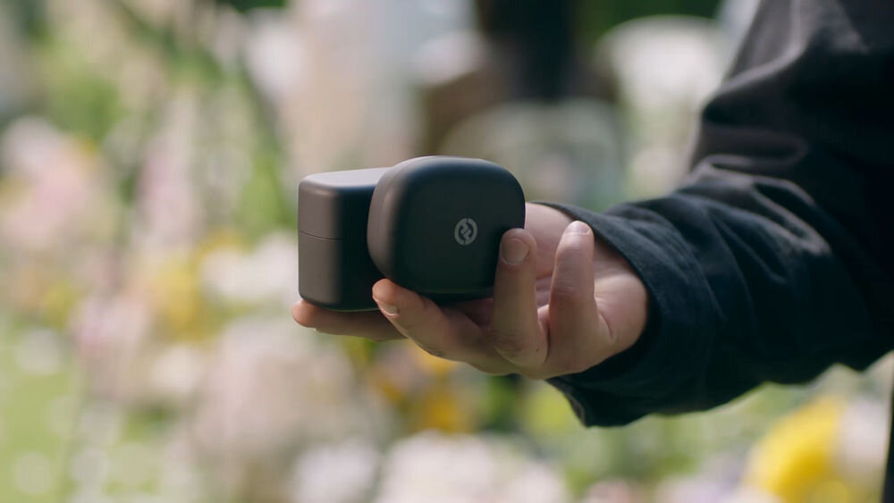 System bezprzewodowy HOLLYLAND Lark Max 2 Ultimate Combo Dłoń trzymająca dwa czarne pudełka mikrofonów MAX 2 na rozmytym tle z kwiatami zasięg do 100 m w linii wzroku adapter gorącej stopki eliminacja plątaniny kabli bezprzewodowe monitorowanie dźwięku ze smartfona dynamiczne sytuacje