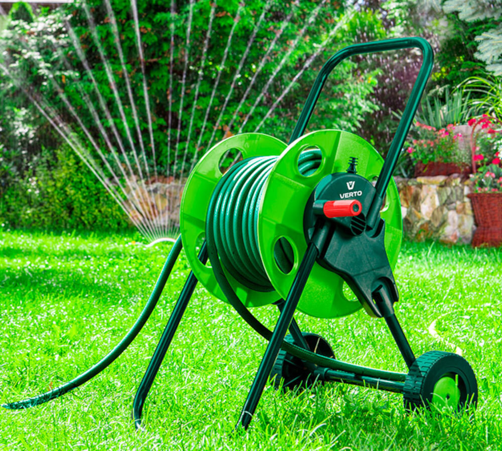 Wąż ogrodowy VERTO Economic 3/4 50 m 15G805, woda, podlewanie, ogród, źródło, w tle zraszacz podlewa trawnik, na pierwszym planie wąż nawinięty na szpule