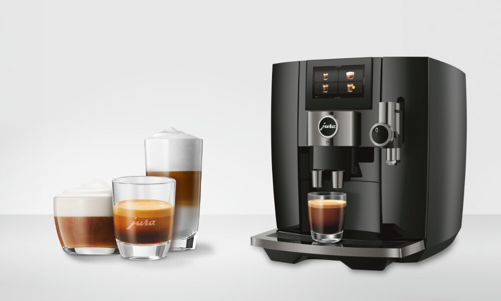 Czarny ekspres do kawy z logo \'jura\' na przednim panelu, obok trzy szklanki z różnymi rodzajami kawy, w tym cappuccino i espresso.
