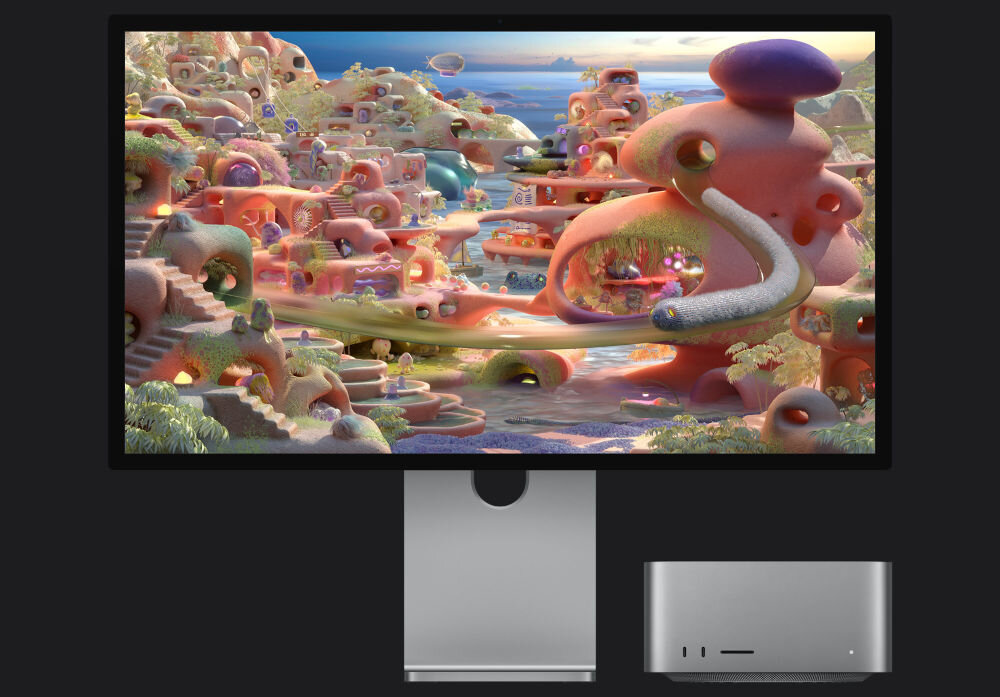 Monitor APPLE Studio Display XDR Monitor profesjonalny wyświetlający kolorową grafikę surrealistycznej krainy, obok którego stoi kompaktowy komputer stacjonarny w srebrnej obudowie.