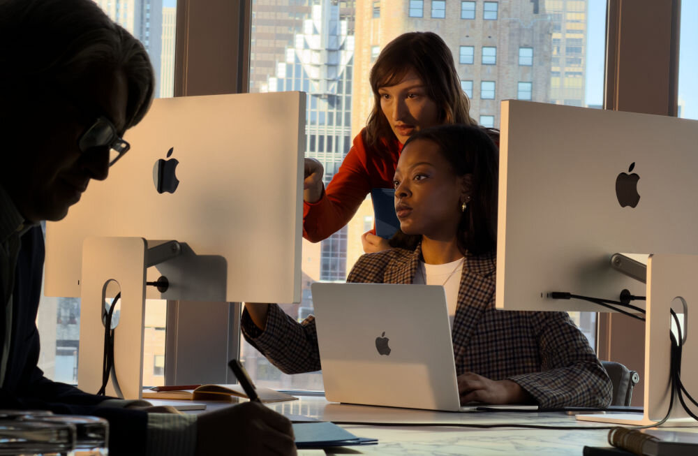 Monitor APPLE Studio Display Trzy osoby pracujące w nowoczesnym biurze przy komputerach Apple Mac; w tle widok na wieżowce w mieście.