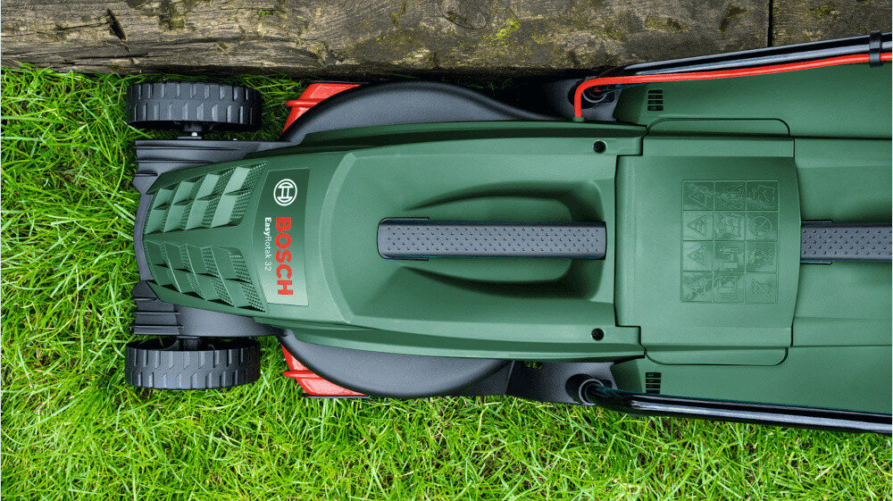 Kosiarka elektryczna BOSCH EasyRotak 32-235 1200 W 320 mm ogród zbliżenie na korpus kosiarki kosiarka prowadzona przy krawężniku trawa widok z góry specjalne grzebienie umieszczone przy korpusie pomagają doprowadzić źdźbła trawy pod nóż dokładne koszenie wzdłuż krawędzi oszczędza czas i wysiłek
