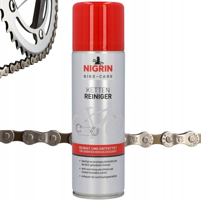 Na obrazie widoczna jest puszka preparatu do czyszczenia łańcucha rowerowego z czerwonym wieczkiem, oznaczona logo \'NIGRIN BIKE-CARE KETTEN REINIGER\'. Obok znajduje się fragment metalowego łańcucha rowerowego oraz zębatki.