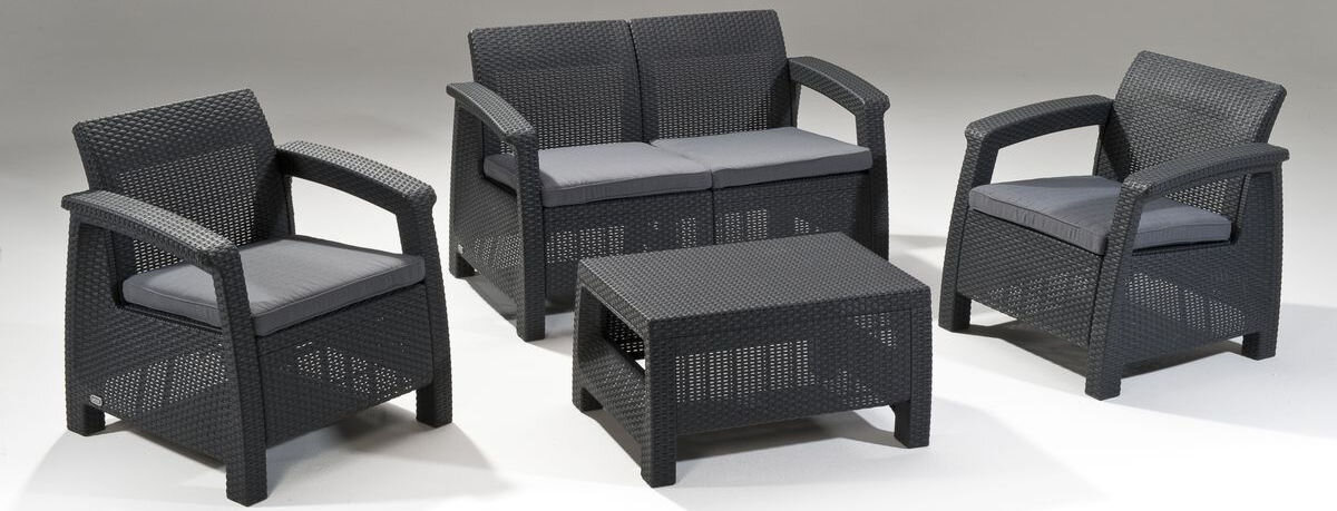 Zestaw mebli ogrodowych składający się z dwóch foteli, dwuosobowej sofy i prostokątnego stolika, wykonany z tworzywa imitującego rattan w kolorze grafitowym. Meble mają szare poduszki na siedziskach.
