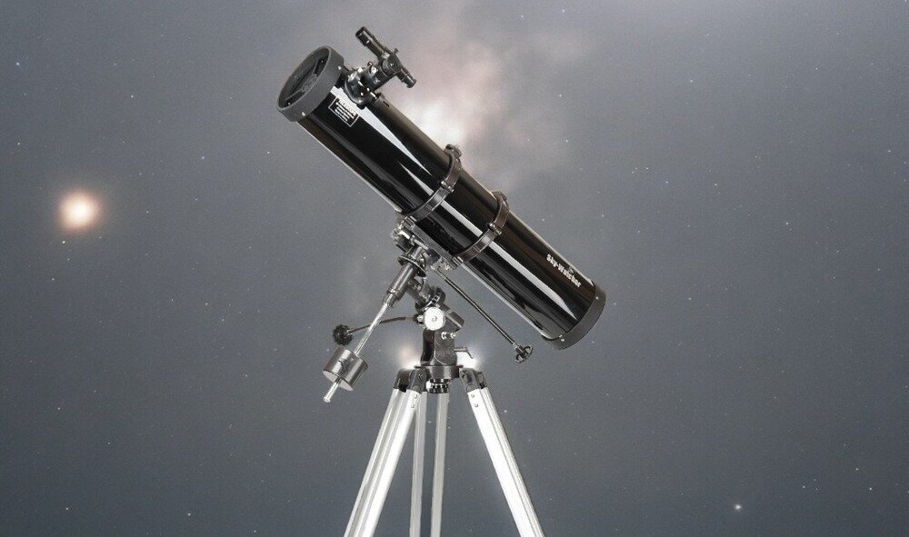 Czarny teleskop na statywie ustawiony na tle gwiaździstego nieba. Na tubusie widoczne jest logo \'Sky-Watcher\'.