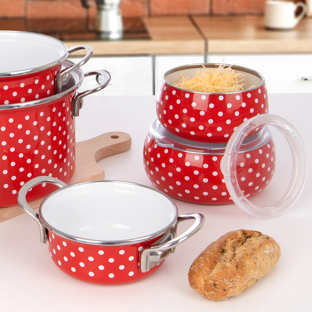 Na obrazie widoczne są czerwone naczynia emaliowane w białe kropki, w tym miska z pokrywką, oraz bochenek chleba na blacie kuchennym. W tle znajduje się drewniana deska do krojenia i elementy kuchenne.