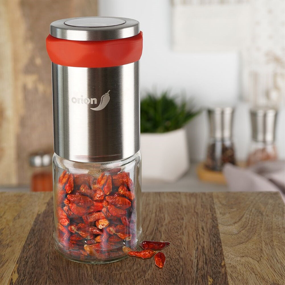 Stalowy młynek z czerwonym akcentem na górze, wypełniony suszonymi papryczkami chilli. Na młynku widoczne jest logo z napisem \'orion\' i symbolem papryczki.