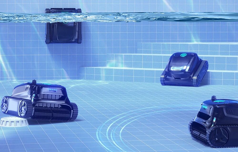 Na obrazie widać trzy roboty do czyszczenia basenów zanurzone w wodzie, poruszające się po dnie basenu wyłożonym niebieskimi płytkami. Roboty mają ciemną obudowę i są wyposażone w gąsienice oraz świecące elementy na górze.