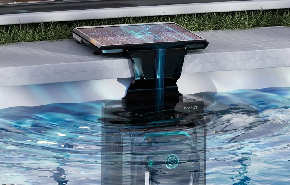 Robot do czyszczenia basenów zanurzony w wodzie przy krawędzi basenu, z panelem słonecznym na górze. Na urządzeniu widoczny jest napis \'WYBOT\'.
