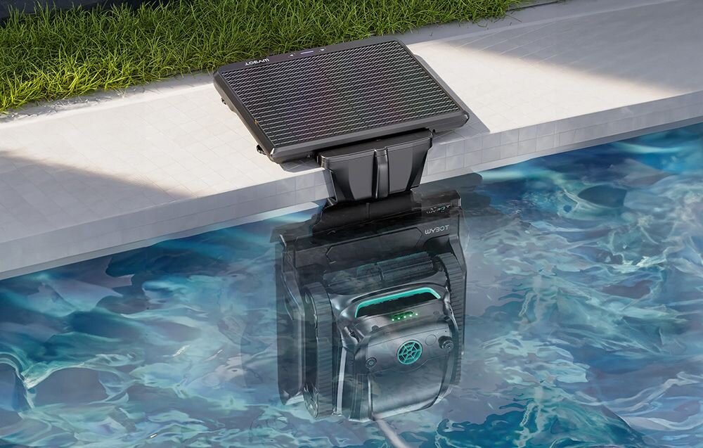 Robot do czyszczenia basenów zanurzony w wodzie przy krawędzi basenu, z panelem solarnym na powierzchni. Na urządzeniu widoczne jest logo \'WYBOT\'.