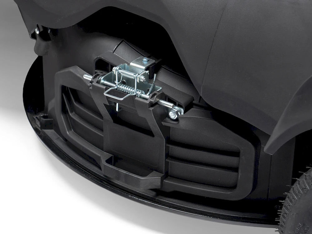 Zbliżenie na część mechanizmu traktora ogrodowego z widocznymi metalowymi elementami i czarną obudową. W tle widać fragment koła z bieżnikiem.