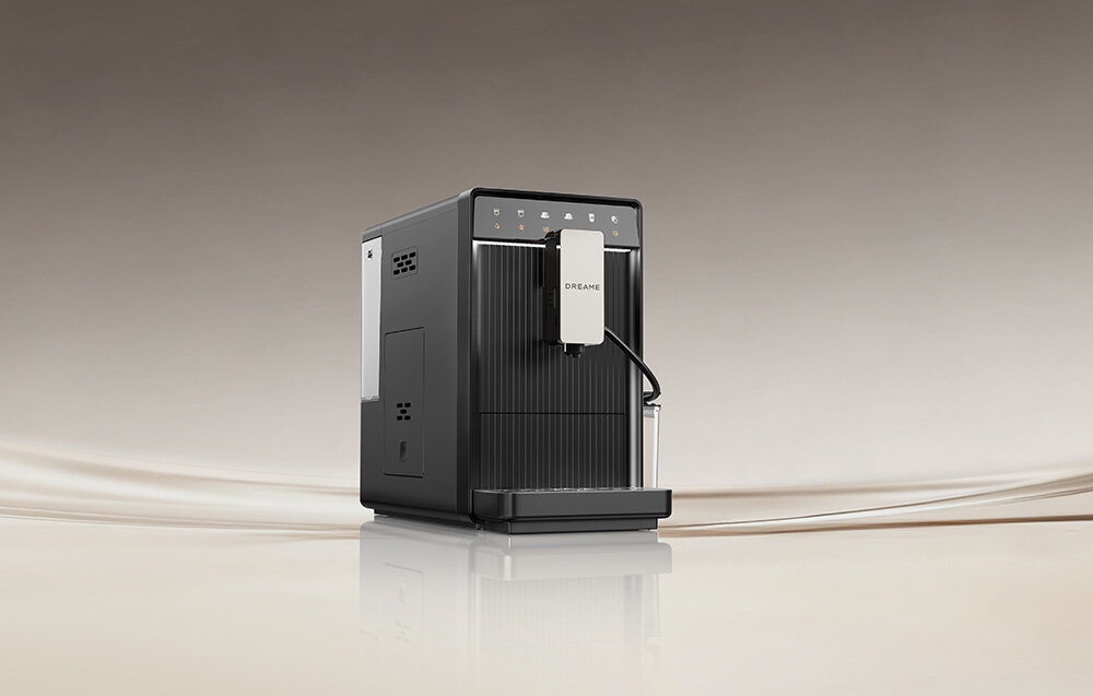 Na obrazie widoczny jest szary ekspres do kawy z logo \'DREAME\' na przednim panelu. Tło jest jednolite, w odcieniach beżu.