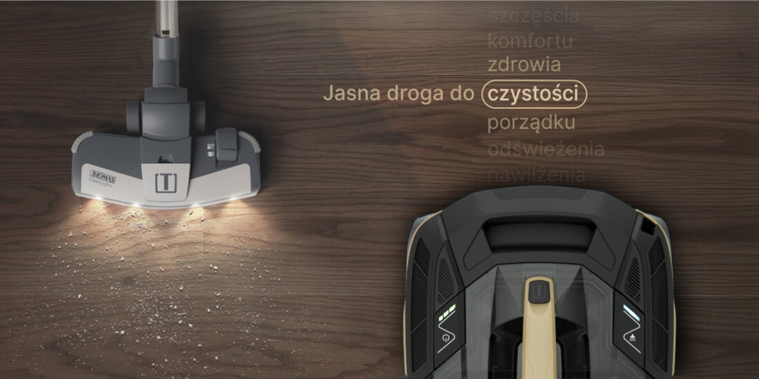 Na drewnianej podłodze widoczna jest głowica odkurzacza z logo THOMAS, emitująca światło na powierzchnię. Obok znajduje się tekst: \'Jasna droga do czystości\'.
