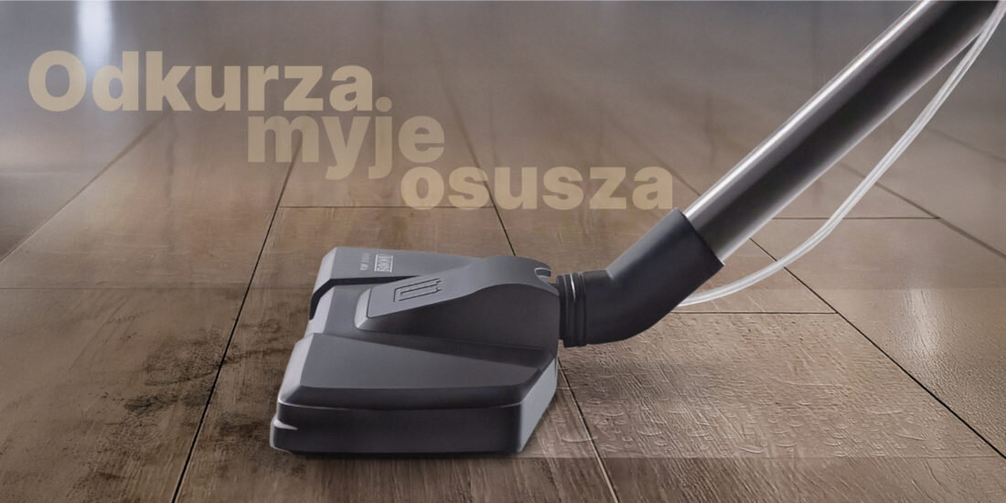 Na obrazie widoczna jest końcówka odkurzacza na drewnianej podłodze. W tle znajduje się tekst: \'Odkurza, myje, osusza\'.