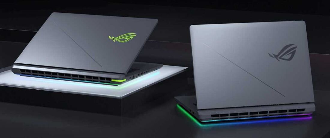 Dwa laptopy z logo ROG na pokrywie, ustawione na ciemnej powierzchni. Oba mają podświetlenie RGB na dolnej krawędzi obudowy.