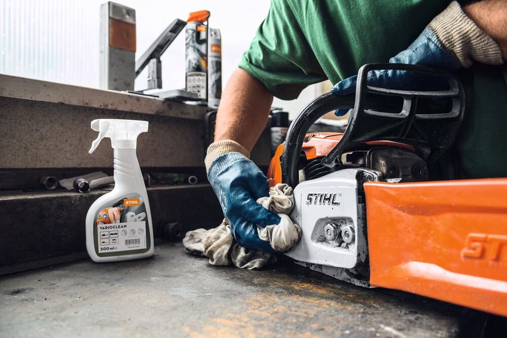 Osoba w rękawicach czyszcząca piłę łańcuchową marki STIHL na stole warsztatowym. Obok znajduje się butelka środka czyszczącego STIHL VariClean 500ml.