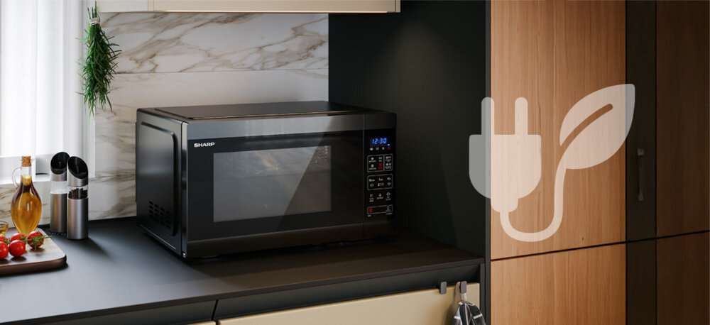 KUCHNIA MIKROFALOWA Z AIRFRY SHARP YC-MA262AE-B Zdjęcie przedstawia czarną kuchenkę mikrofalową Sharp ustawioną na blacie w kuchni, z widocznym panelem sterowania i zegarem 12:30. Zdjęcie przedstawia także duży, jasny piktogram wtyczki z listkiem na drewnianej zabudowie po prawej stronie, symbolizujący energooszczędność urządzenia tryb eco energooszczędne gotowanie sharp yc-ma262ae-b air fry 1500 w niższe zużycie energii oszczędność prądu ekonomiczne gotowanie