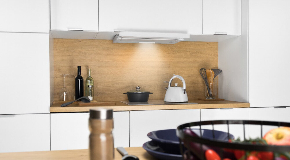 OKAP AKPO WK-7 Light Glass Eco 60 Na zdjęciu 1.jpg przedstawiono kuchnię w czarno‑białej zabudowie z czarnym, szklanym okapem skośnym zawieszonym nad płytą grzewczą i piekarnikiem do zabudowy. Po prawej stronie widać lodówkę w kolorze inox oraz stół z wazonem czerwonych tulipanów, co dodaje aranżacji przytulnego charakteru