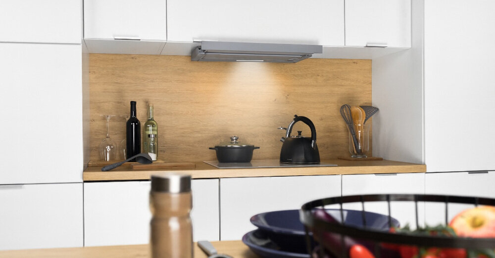 OKAP AKPO WK-7 Light Glass Eco 60 Na zdjęciu 1.jpg przedstawiono kuchnię w czarno‑białej zabudowie z czarnym, szklanym okapem skośnym zawieszonym nad płytą grzewczą i piekarnikiem do zabudowy. Po prawej stronie widać lodówkę w kolorze inox oraz stół z wazonem czerwonych tulipanów, co dodaje aranżacji przytulnego charakteru