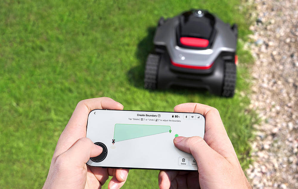 Robot koszący DREAME A3 AWD Pro 5000 trawnik robot na trawie na pierwszym planie osoba z telefonem w dłoni wysokość koszenia można dostosować w aplikacji Dreamehome w zakresie od 3 do 10 cm radzi sobie również z gęstą trawą o wysokości nawet 20 cm zmiana ustawień odbywa się błyskawicznie za pomocą jednego kliknięcia szerokość robocza wynosi 40 cm