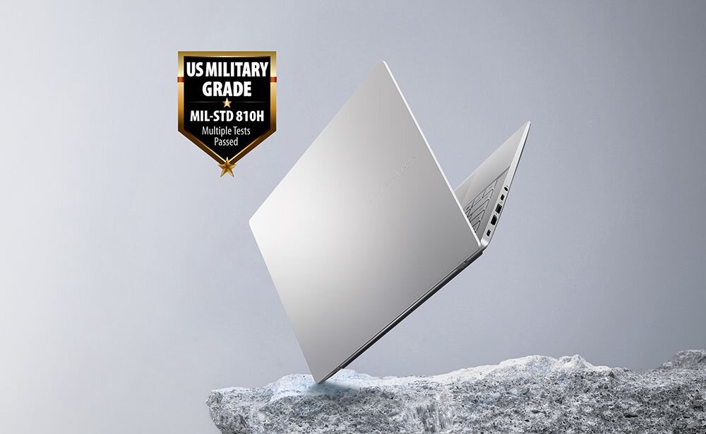 Laptop ASUS Vivobook S14 w kolorze srebrnym unoszący się nad powierzchnią o fakturze skały, na tle plakietka „US Military Grade MIL-STD 810H – Multiple Tests Passed”, symbolizująca wytrzymałość konstrukcji zgodną z normą wojskową.  - Wytrzymałość klasy wojskowej MIL-STD-810H